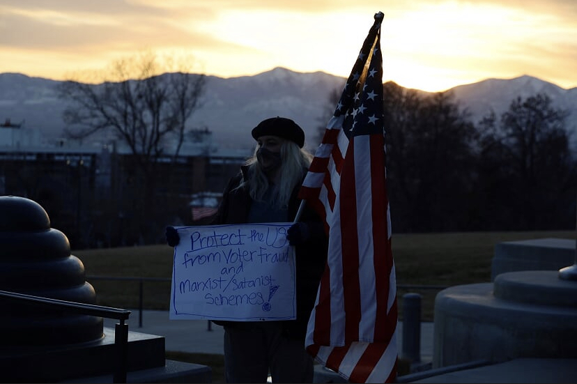 Trump supporter holds sign about voter fraud and “Marxist/Satanist” schemes